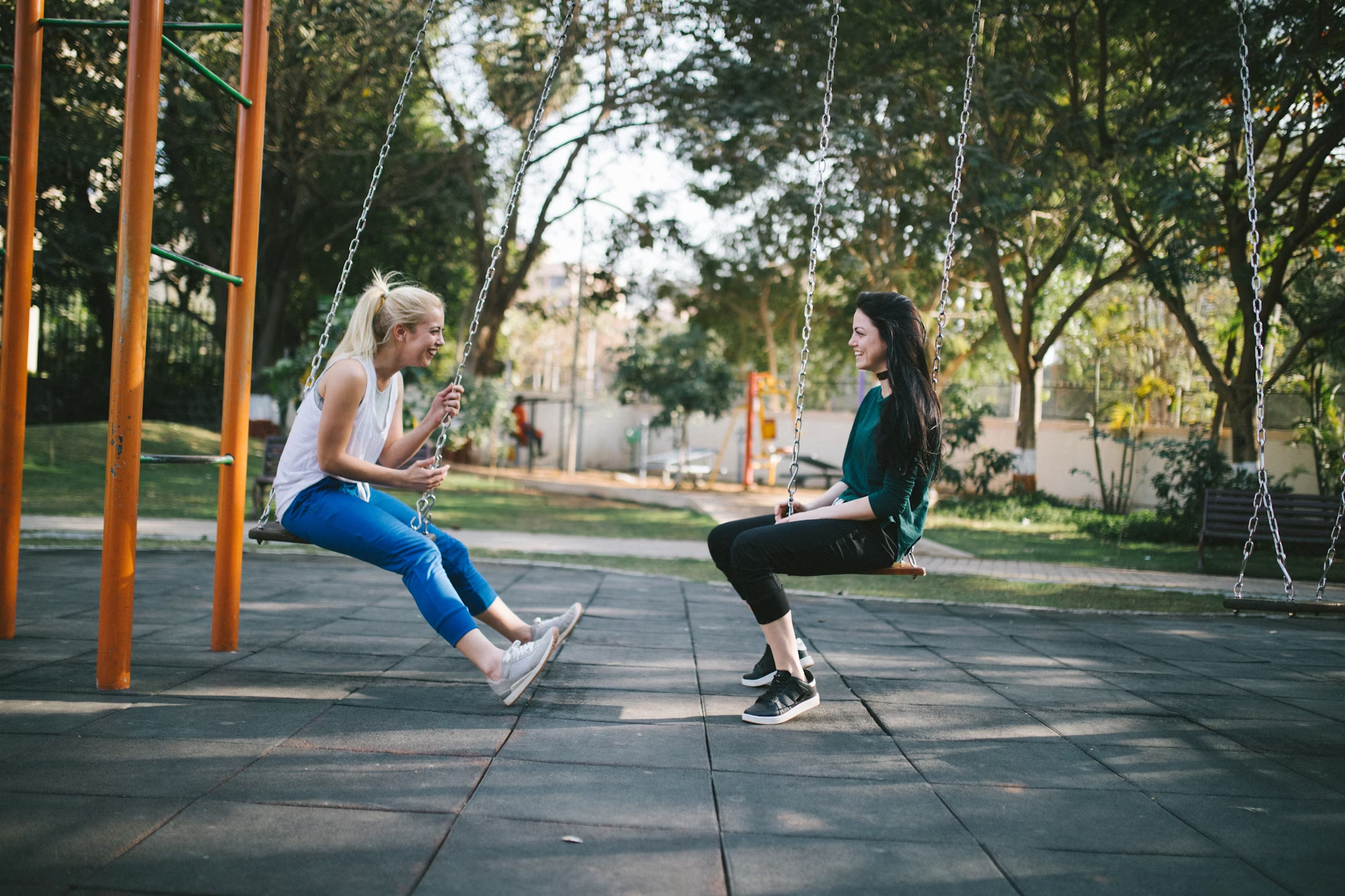 Deux filles jouant sur une balançoire dans un parc entouré de nombreux équipements en acier inoxydable.